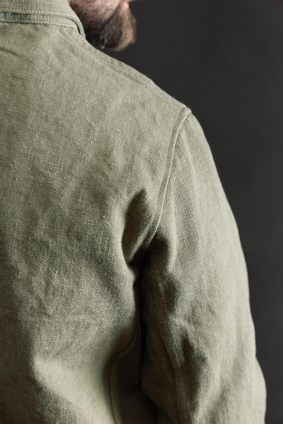 Close-up of back shoulder and upper sleeve on olive selvedge denim jacket, male model 5'9 165lbs athletic build