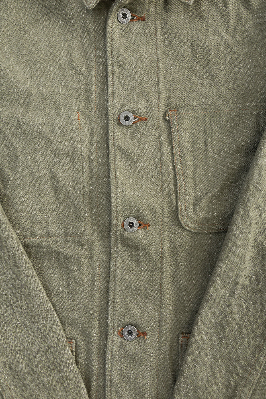 Close-up of front selvedge olive denim jacket, showing buttons, chest pocket, and fabric texture.