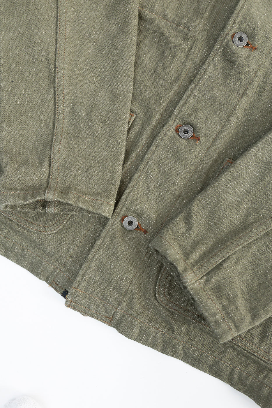 Close-up of front lower section, cuff, and buttons on olive green selvedge denim coverall jacket.