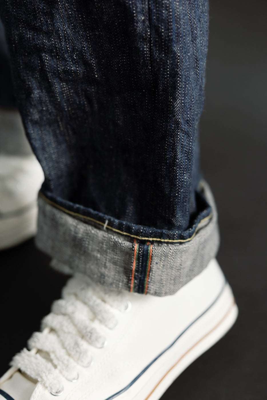 Close-up of cuffed selvedge denim hem on men's jeans, showing fabric texture and stitching, front side.