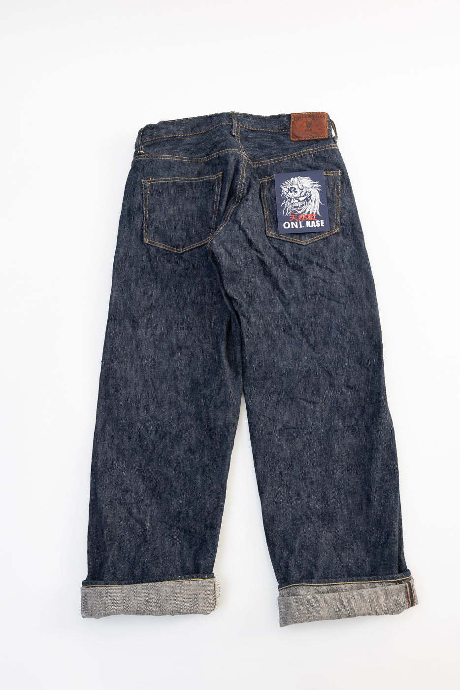 Flat lay of wide straight ONI KASE selvedge jeans, back view, showing rear pockets and logo patch