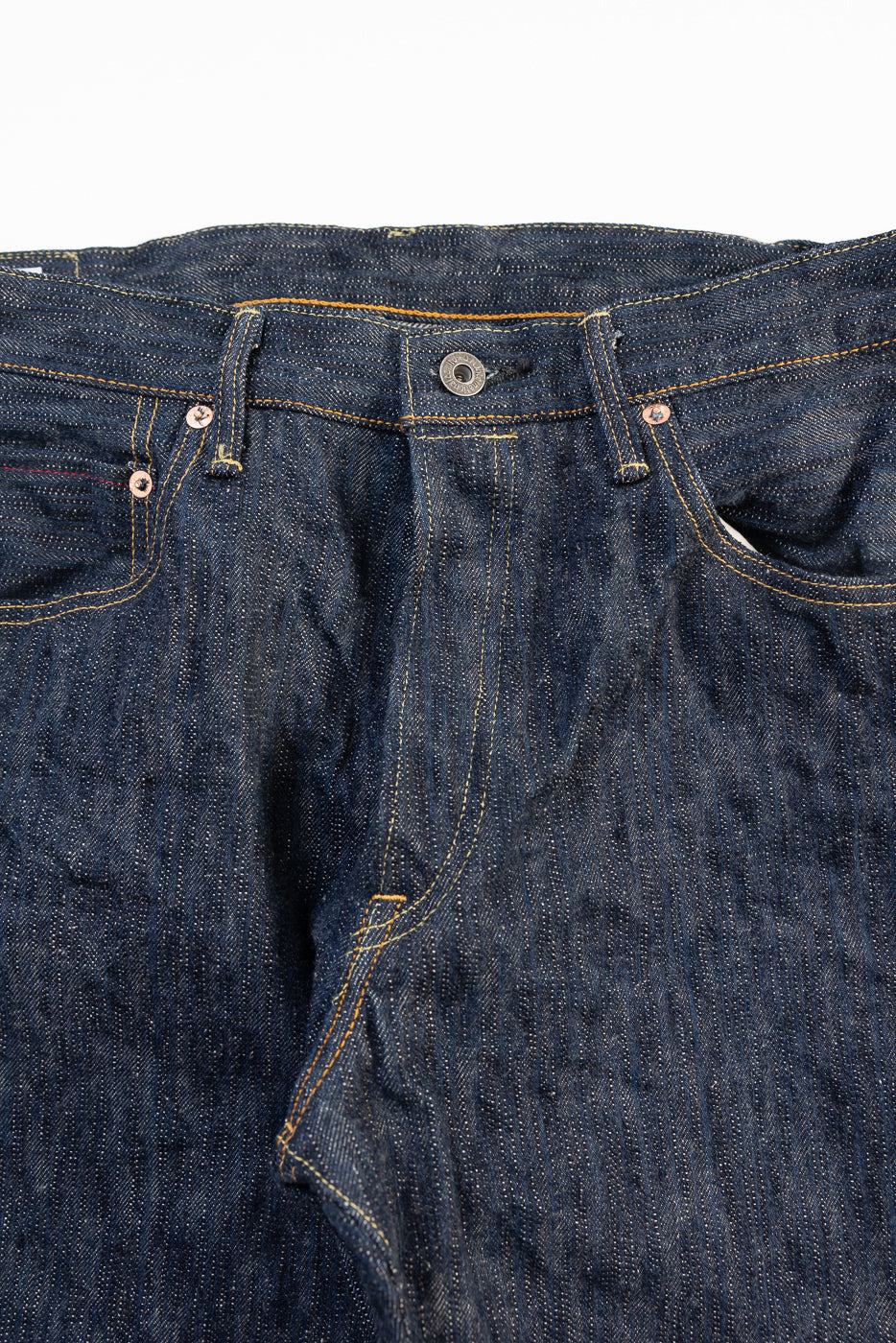 Close-up of front waist and pockets of ONI KAS 16oz selvedge denim jeans, highlighting button, rivets, and textured indigo fabric.