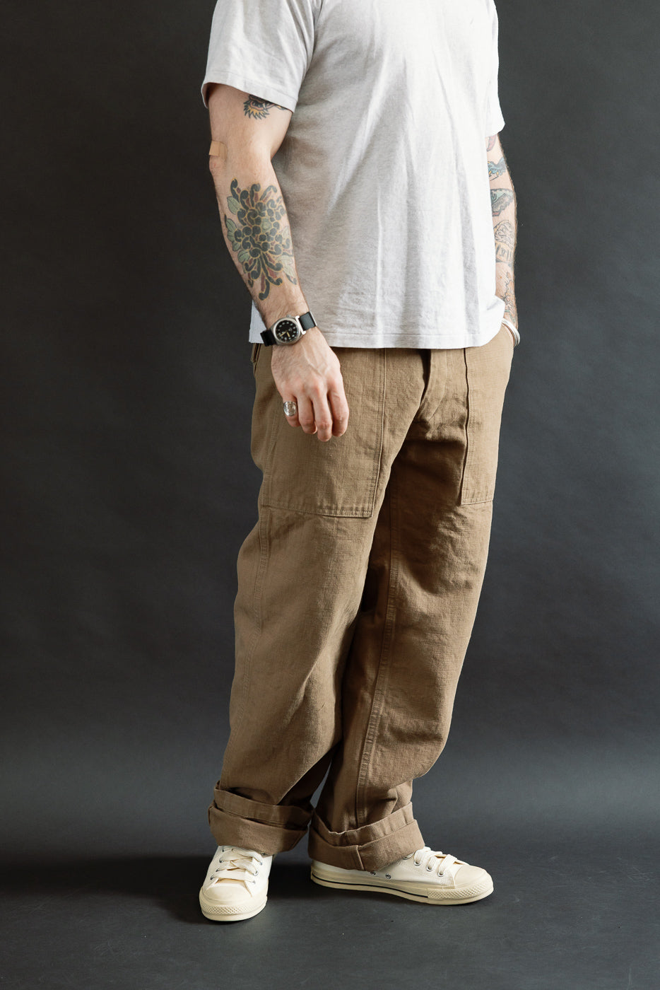 207-HOX-BRK - 13oz Brown Khaki Sulfur Dyed Heavy Oxford Baker Pants feature a wide straight cut and patch pockets, styled with off-white sneakers and a tucked white T-shirt.