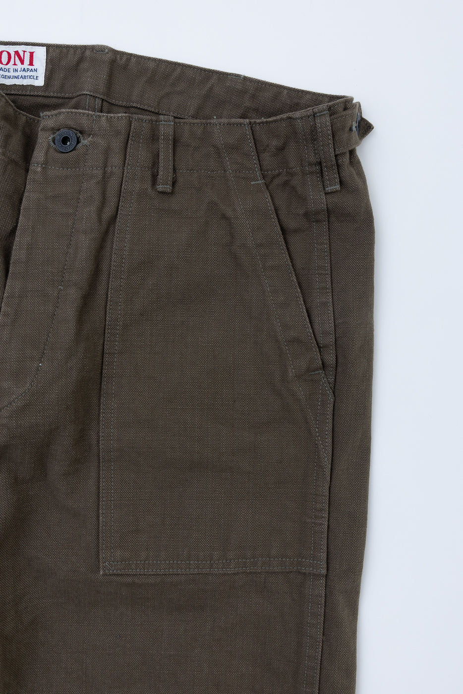 Close-up of 207-HOX-OLB 13oz Olive Khaki Sulfur Dyed Heavy Oxford Baker Pants, showcasing the waistband with button closure, belt loops, adjuster tab, and large front patch pocket with a Made in Japan label.
