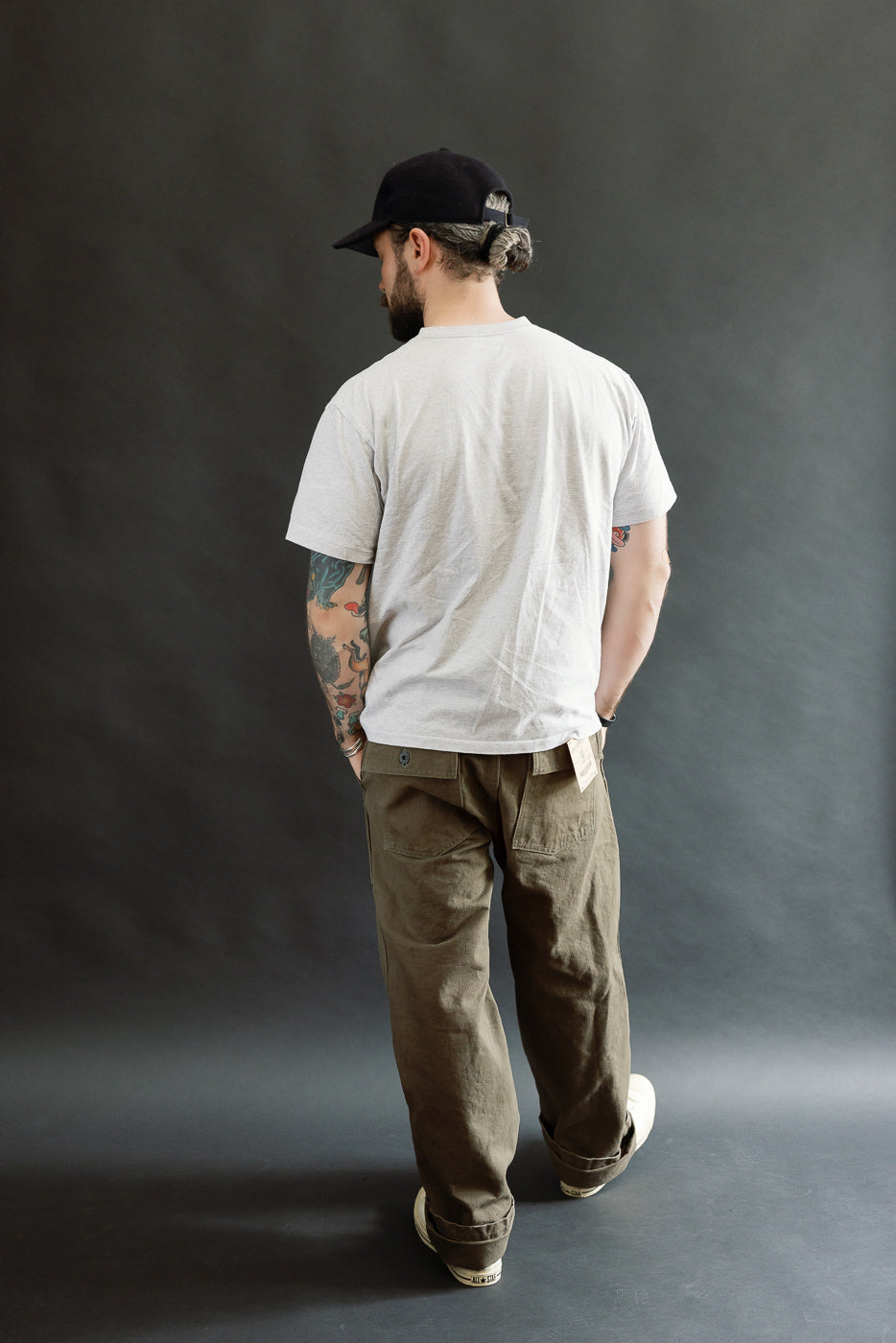 Adult male model wearing 207-HOX-OLB Baker Pants in olive khaki, showcasing a wide straight cut with a high rise and relaxed waist. The pants have a textured, sulfur-dyed finish and original engraved buttons.
