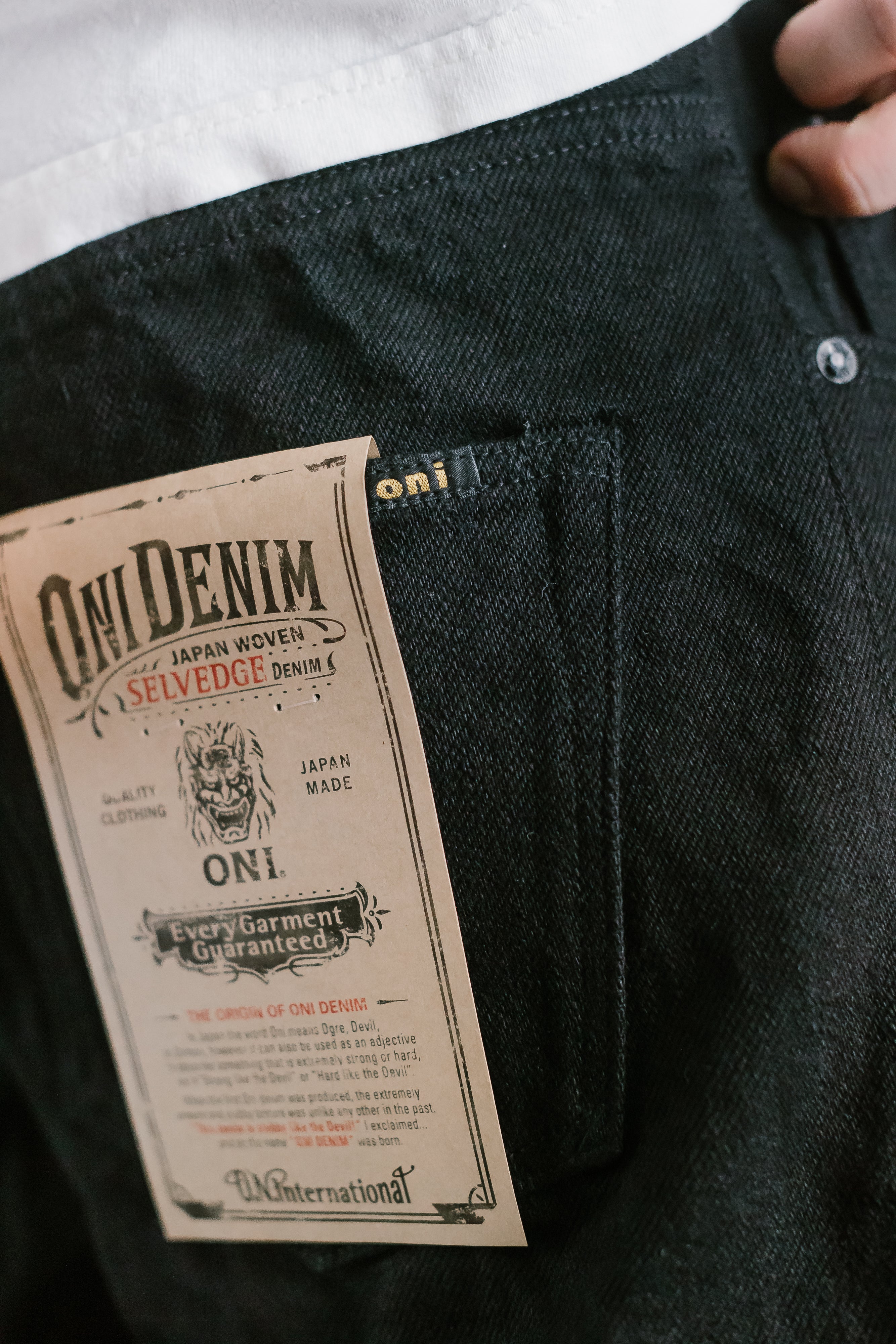 Close-up of Oni Denim selvedge jeans tag, showing Japan-woven fabric details and brand label on dark denim
