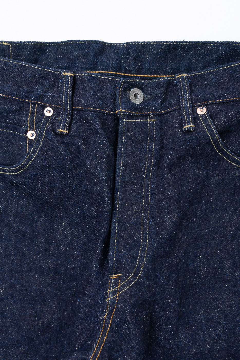 Close-up front view of the waistband and fly of dark indigo selvedge denim jeans.