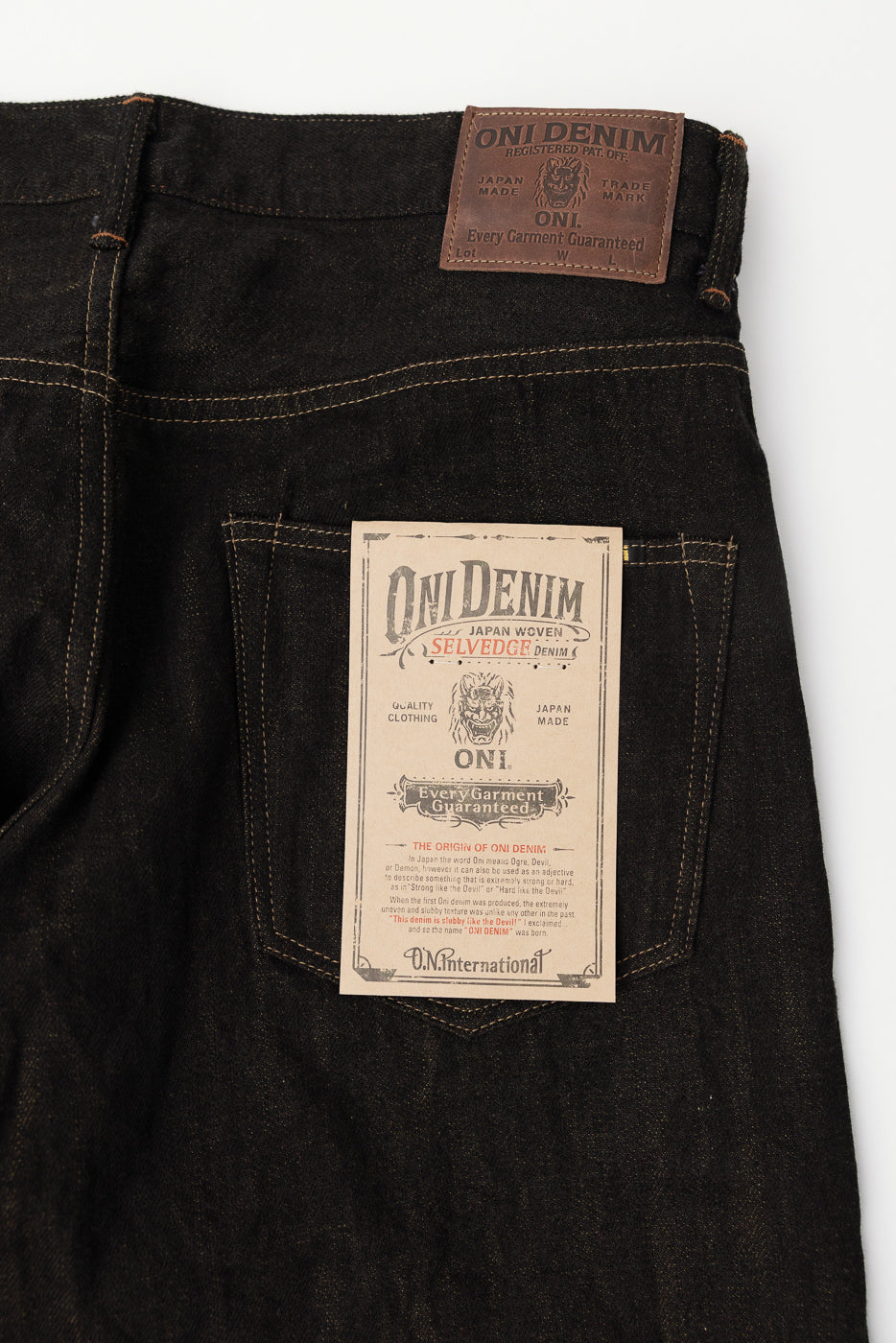 Close-up of back side of ONI Denim black olive selvedge jeans showing leather patch, pocket, and tag.