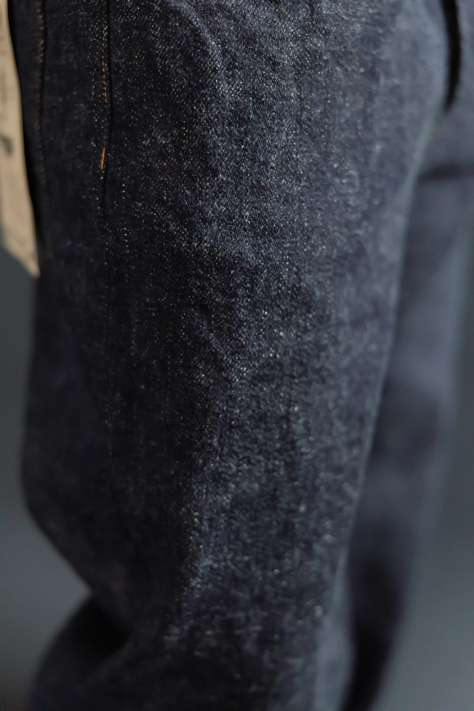 Close-up of dark indigo selvedge denim jeans front thigh, showing textured fabric detail