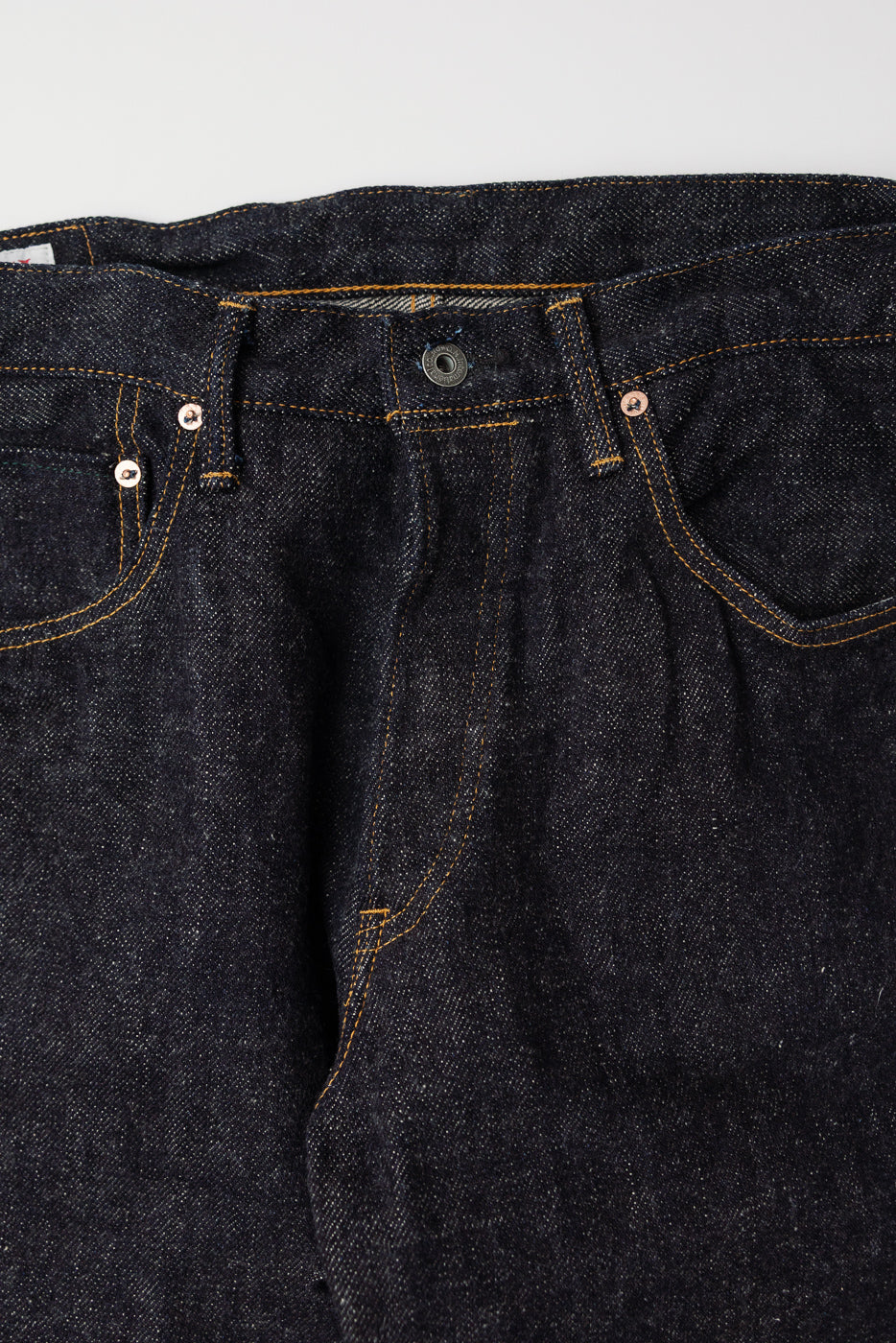 Close-up front view of dark indigo selvedge jeans waist, button, and stitching details