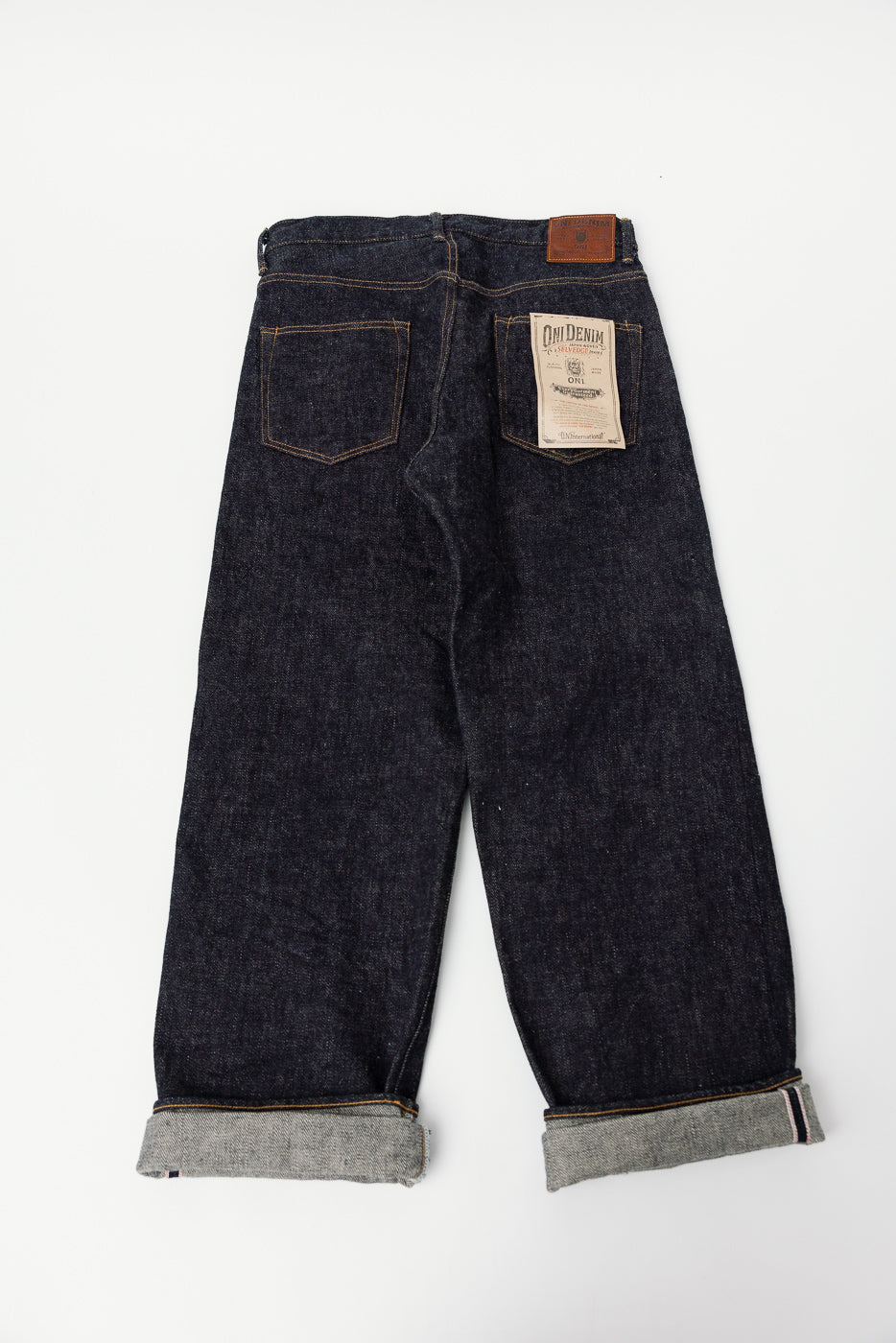 Back view flat lay of ONI Denim 20oz dark indigo selvedge jeans, showing pockets, tags, rolled cuffs.