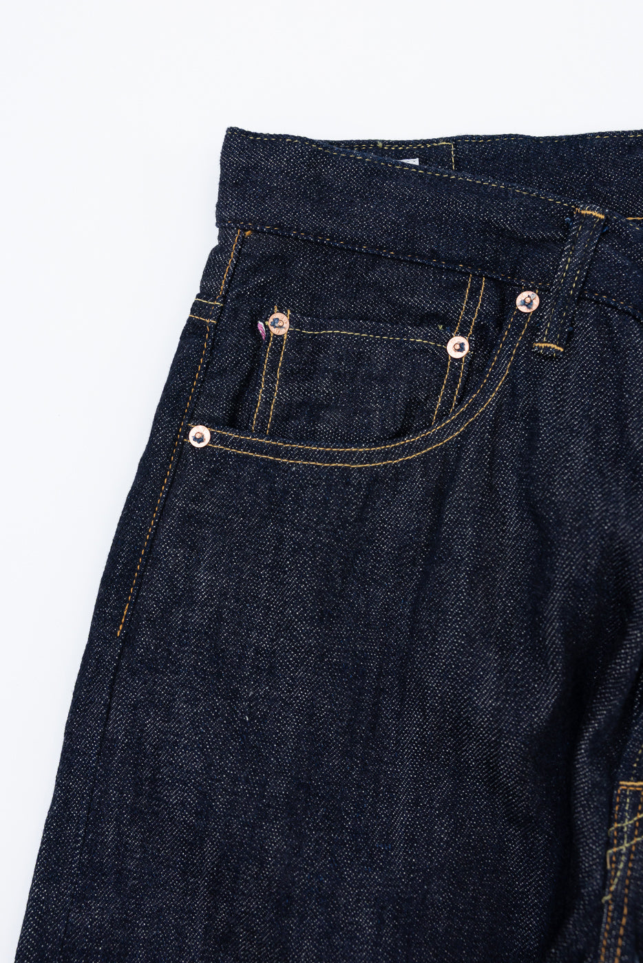 Close-up front view of dark selvedge denim jeans showing front pocket, copper rivets, and yellow stitching detail.