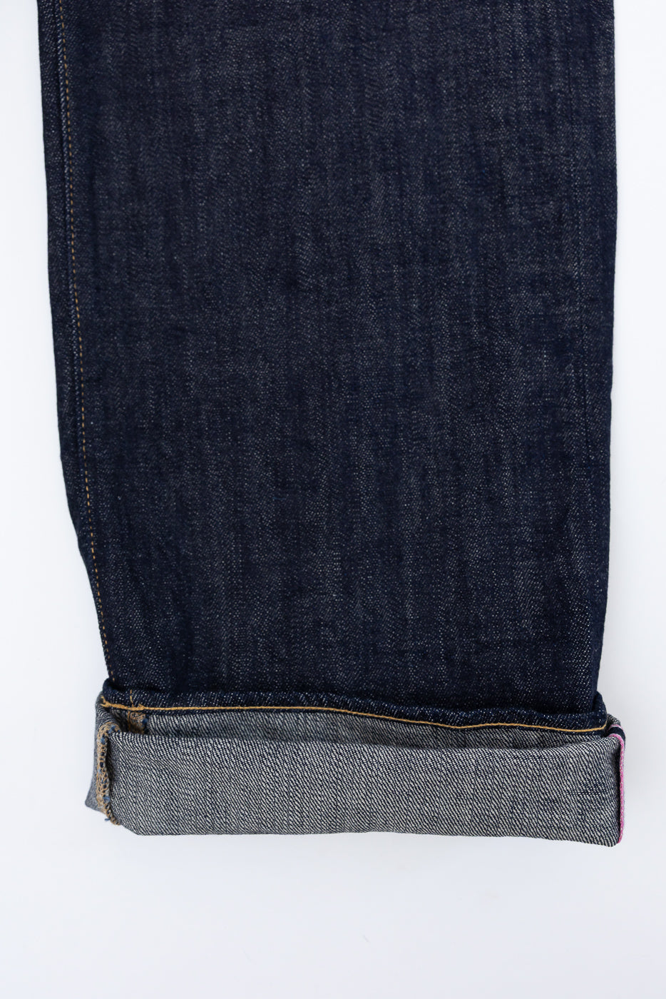 Close-up front view of dark selvedge denim jeans leg with cuffed hem, showing raw edge and contrast stitching detail