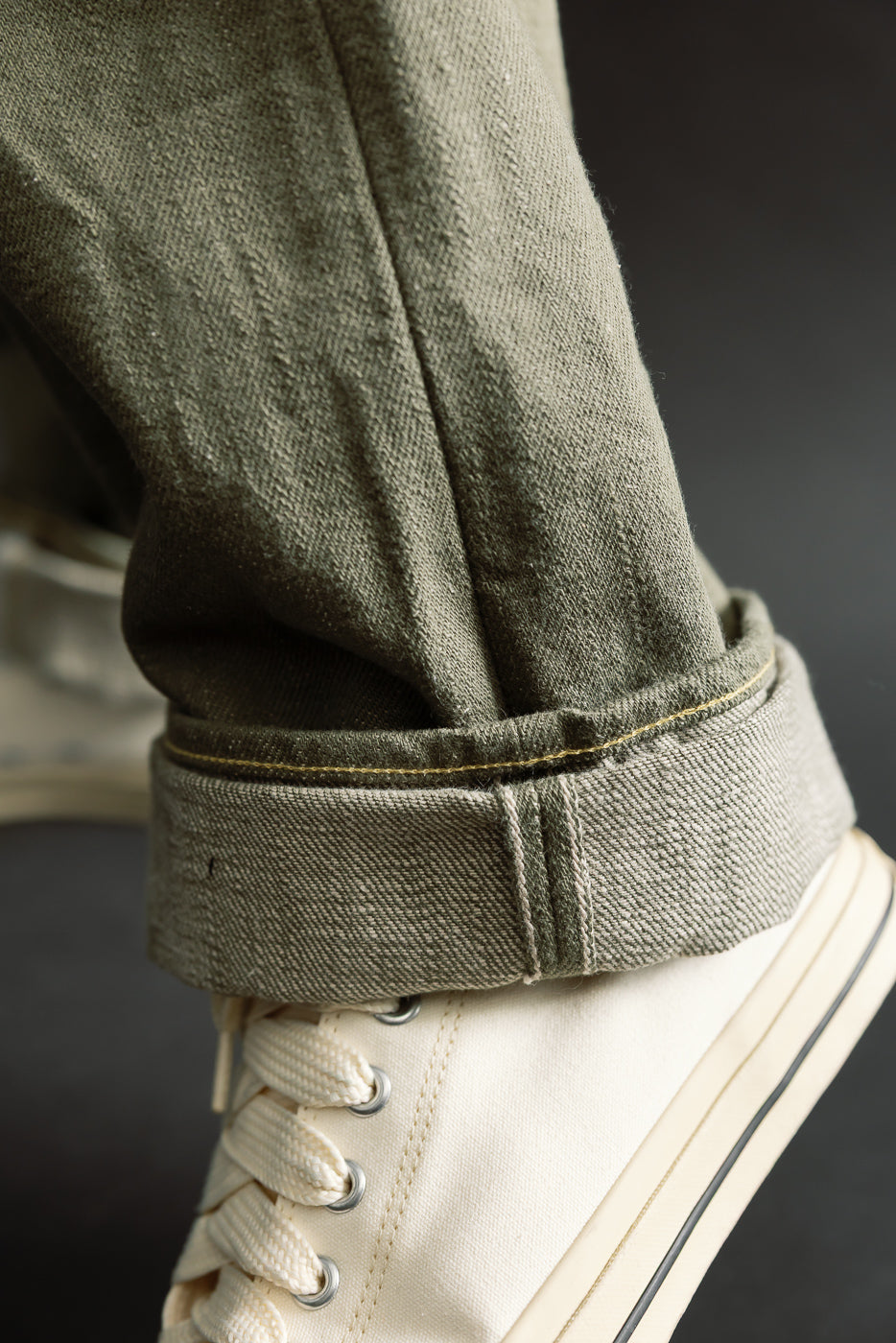 Close-up of cuffed olive selvedge denim jean hem showing fabric texture, worn by male model.