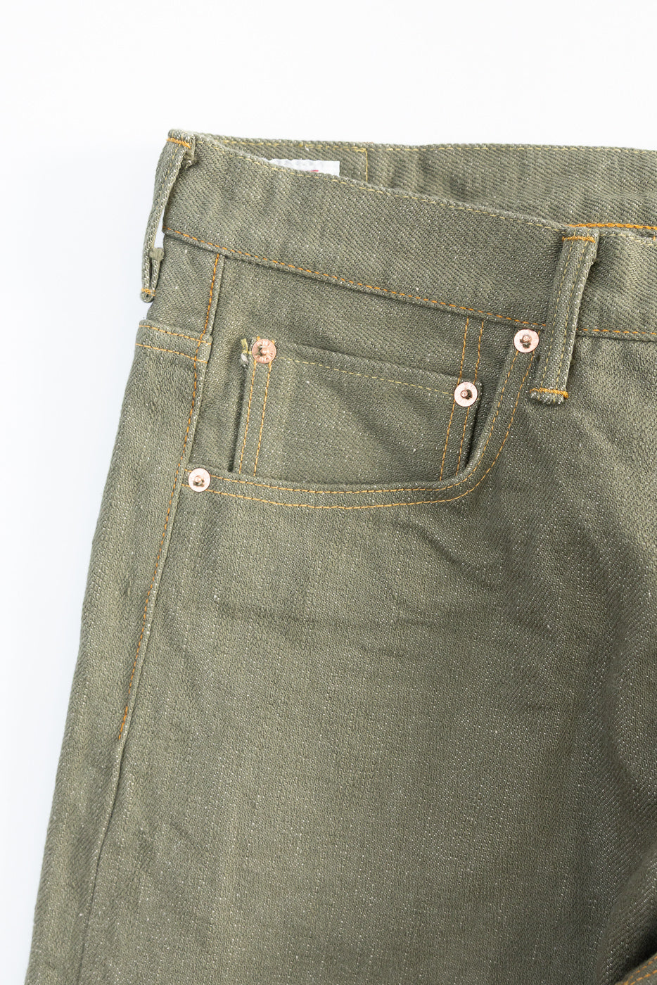Close-up of front left upper section of olive selvedge denim jeans showing pocket, rivets, and fabric texture