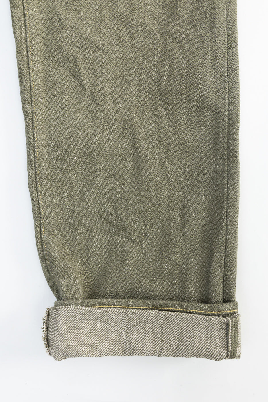 Close-up of front left leg hem of olive green selvedge denim jeans, cuffed to show selvedge edge.
