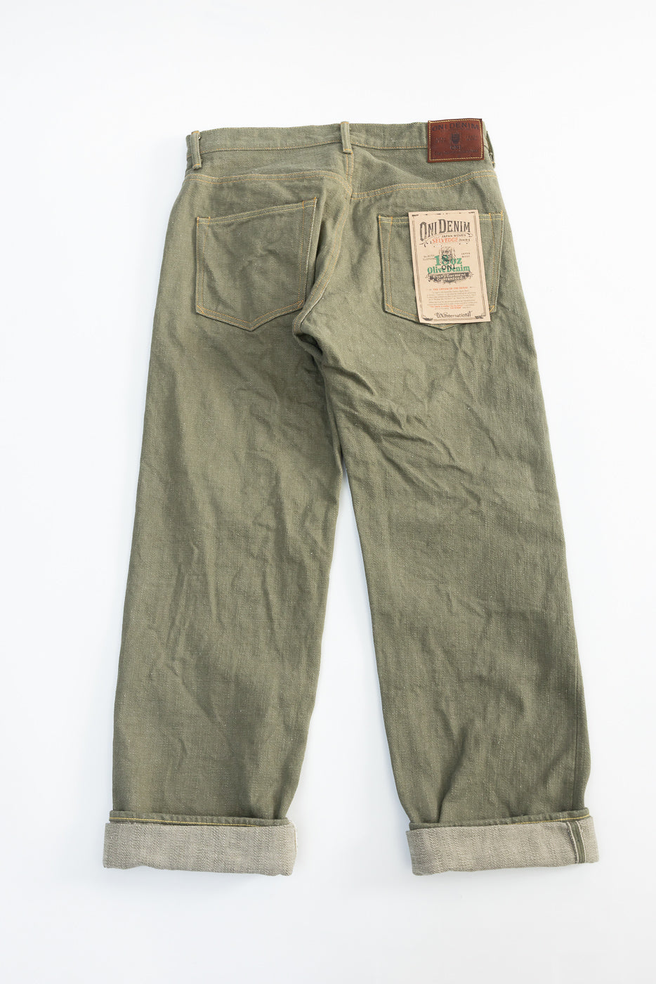 Flat lay of back side olive selvedge denim jeans, showing rear pockets, tags, and cuffs.