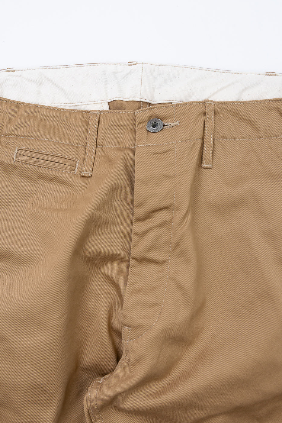 Close-up front view of tan chino pants showing button closure, belt loops, and fabric texture