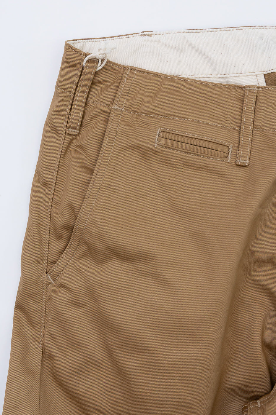 Close-up of tan chino pants front, showing button fly, belt loops, and pocket details
