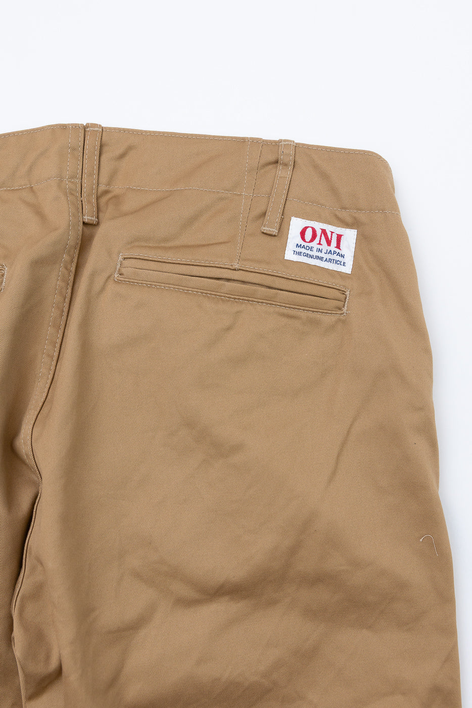 Close-up back view of tan work pants showing ONI brand tag, rear pocket, and stitching detail