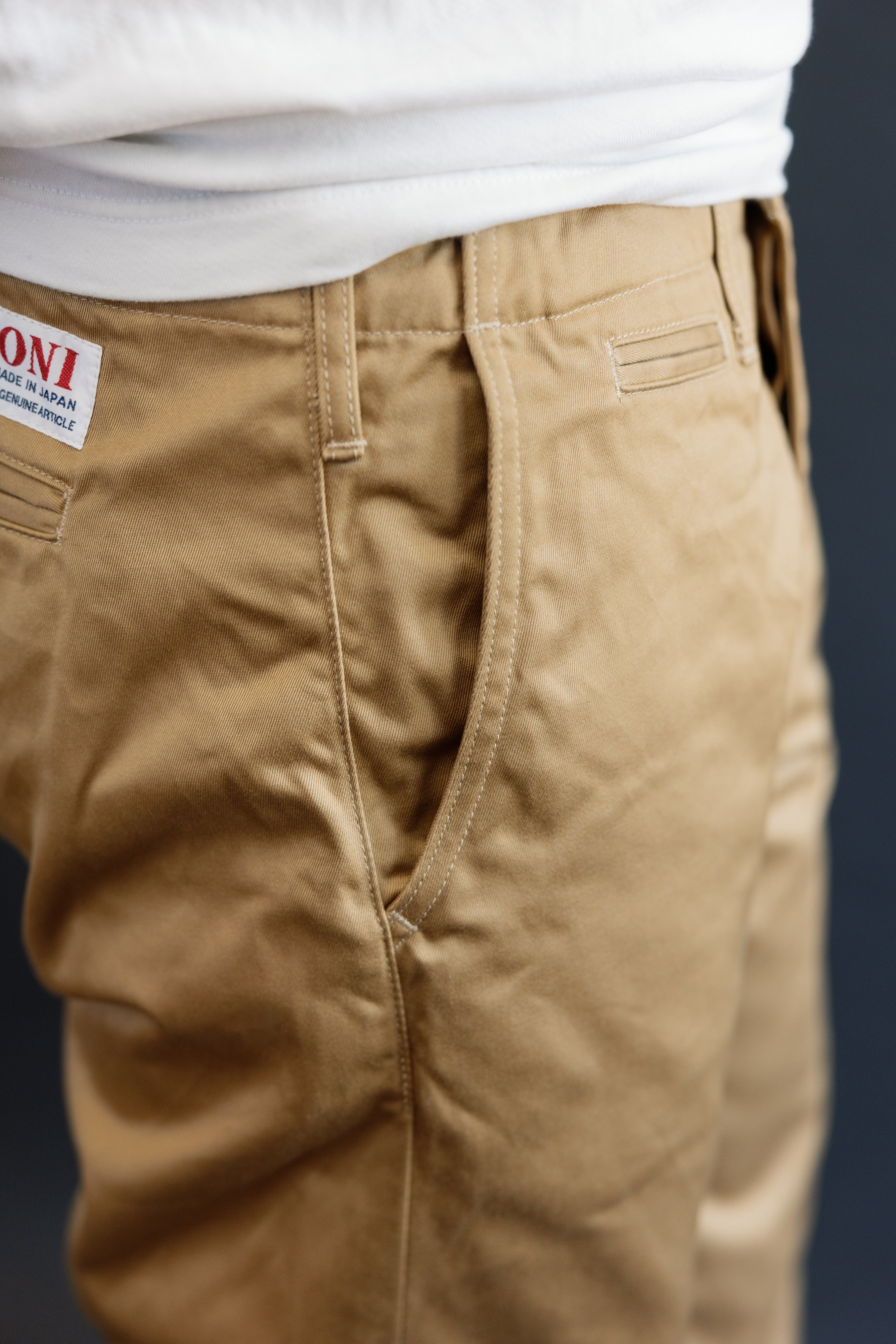 Close-up of male model's back, showing tan chinos with 'ONI' tag, athletic build, 5'9