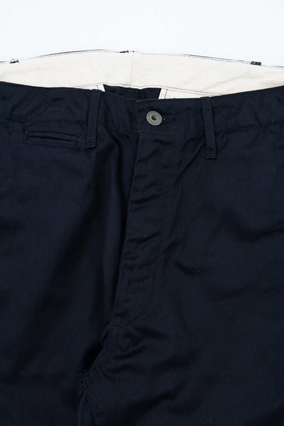 Close-up front view of dark navy chinos showing button closure, belt loops, and cream lining.