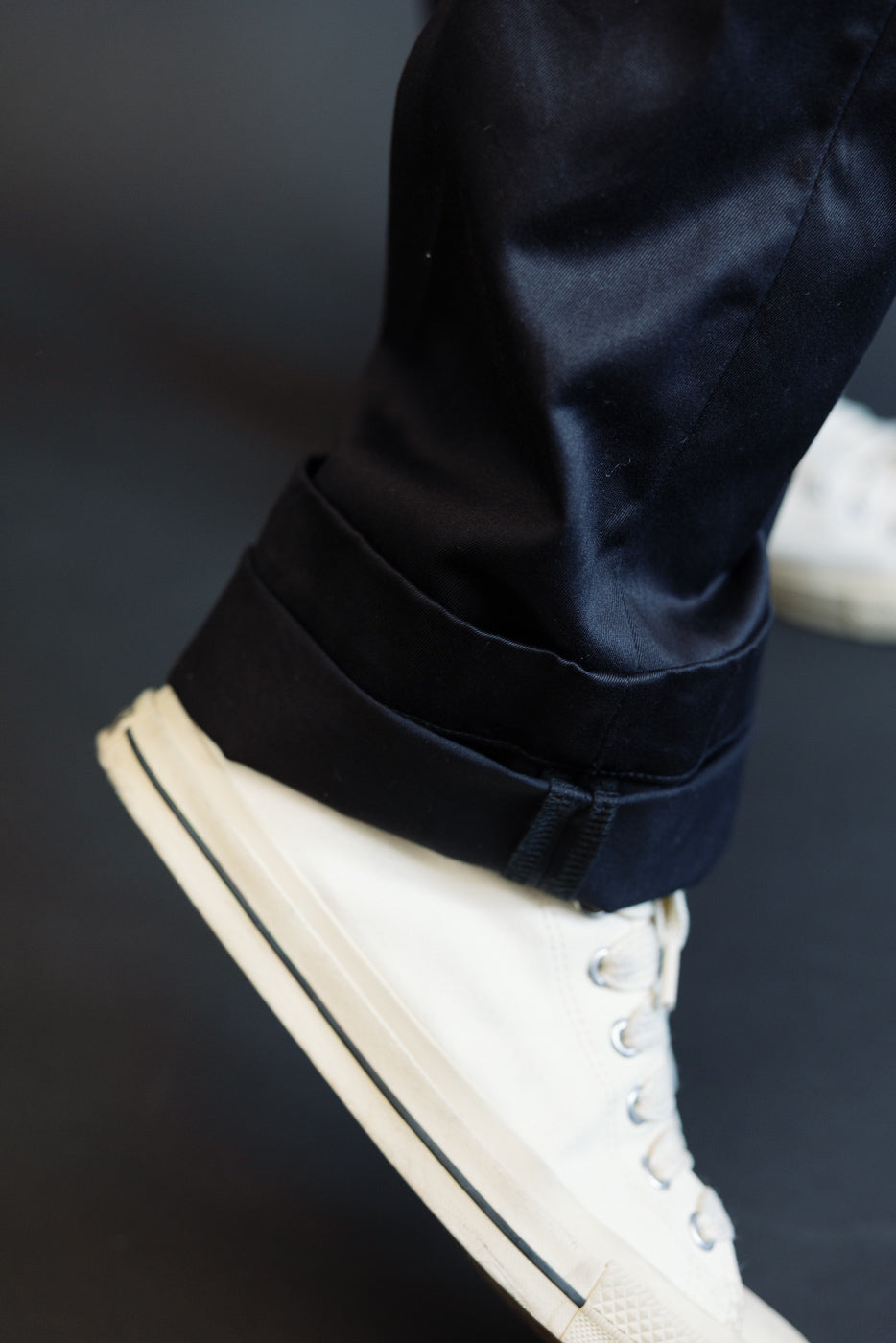 Close-up of male model's cuffed black selvedge pants hem, showing fabric texture and white sneaker pairing