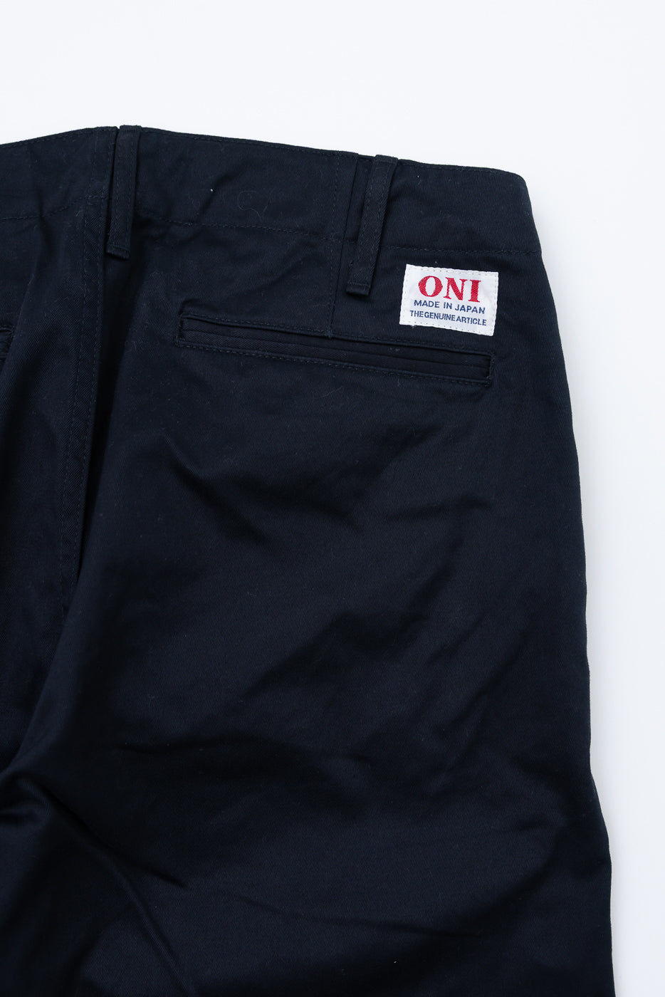 Close-up back view of dark navy chinos showing ONI brand tag, back pocket, and waistband detail