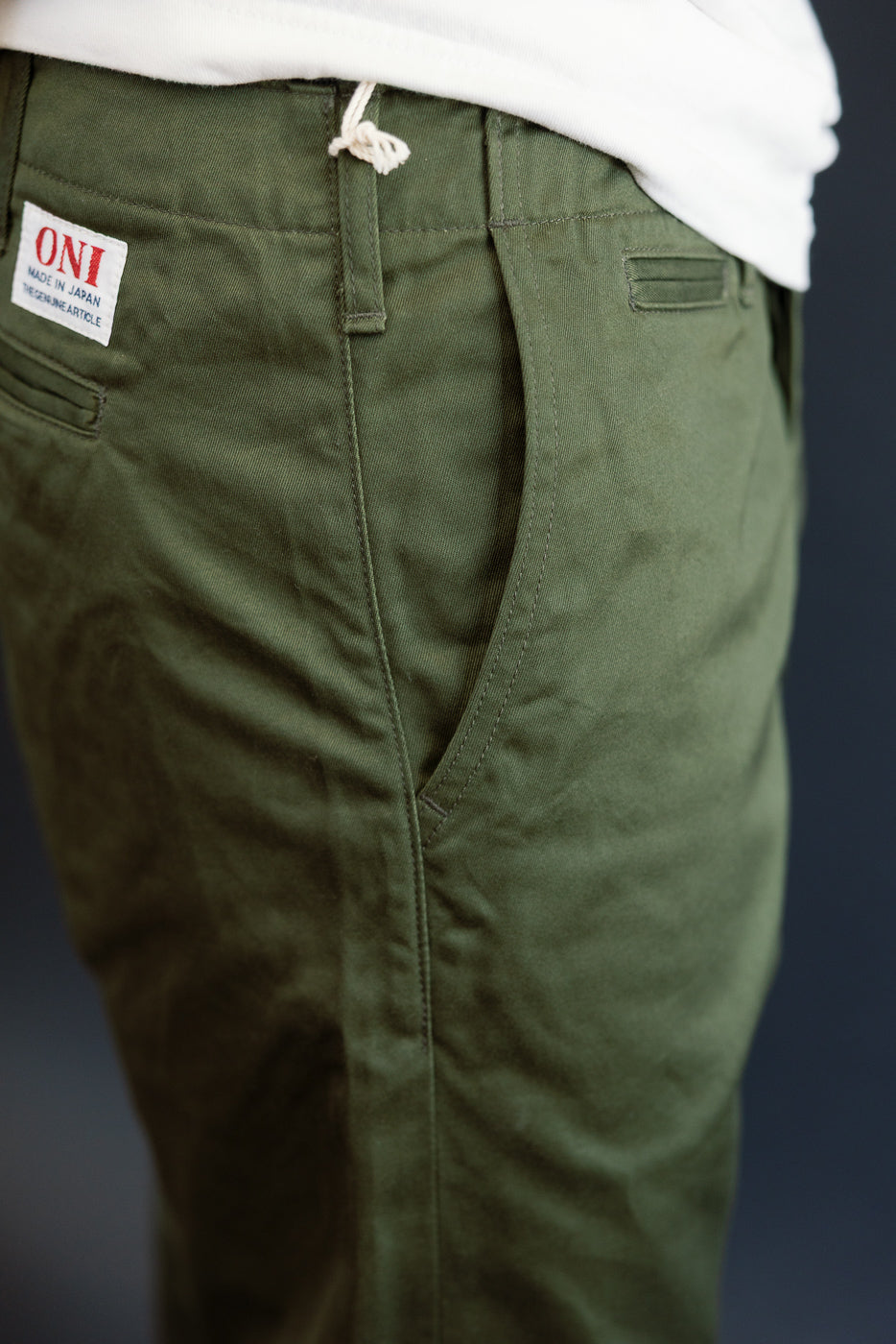 Close-up of olive green pants front, showing ONI tag, drawstring waist, and fabric texture on male model.