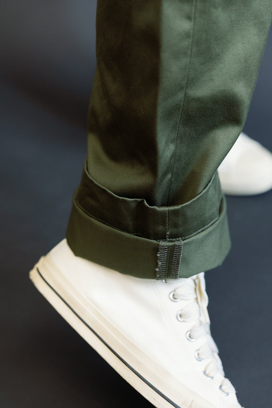 Close-up of olive green pants hem with cuffed detail, worn by male model, paired with white sneakers