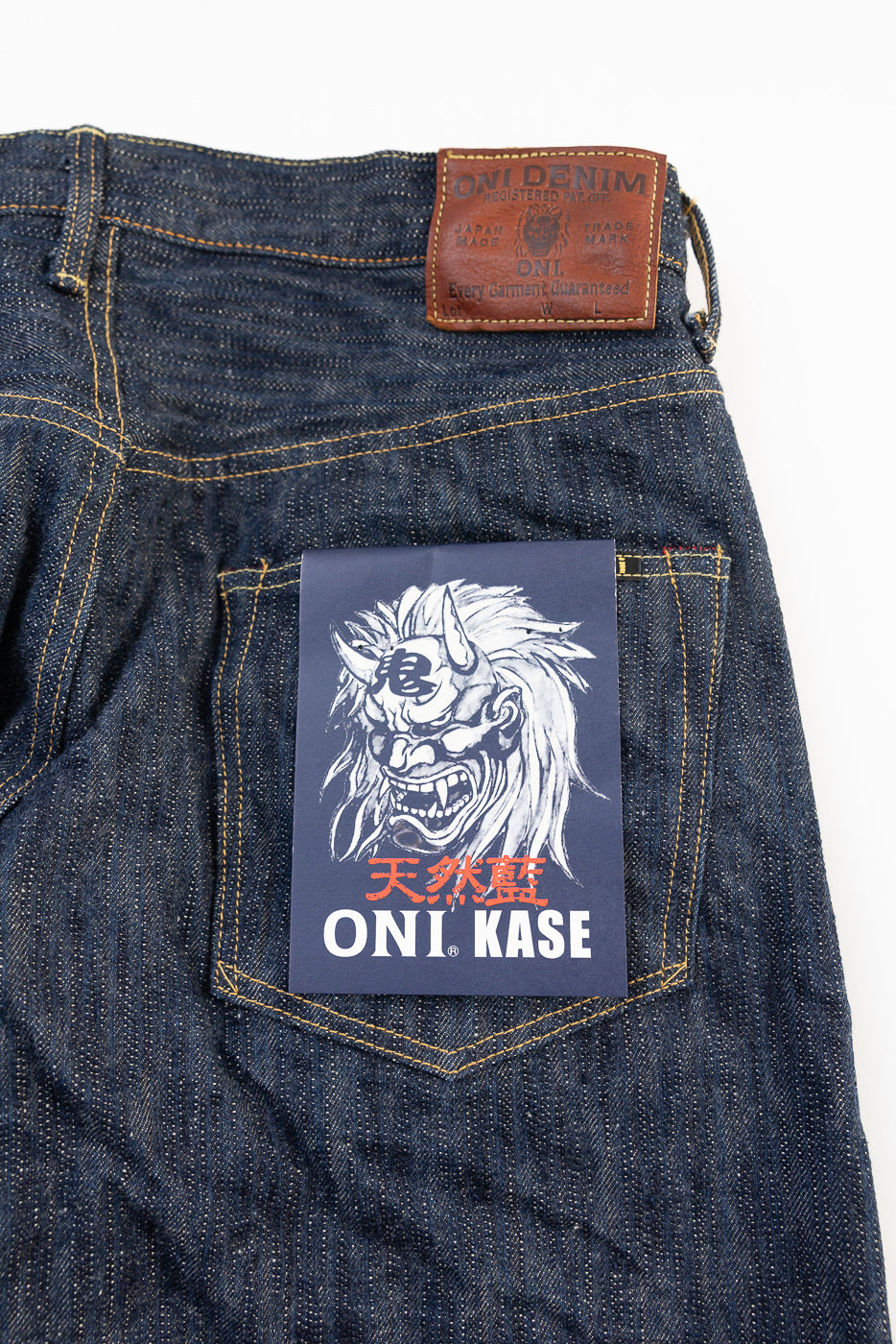 Close-up of ONI Denim Kase selvedge jeans back, showing leather patch, pocket, fabric texture, and ONI KASE branded card.