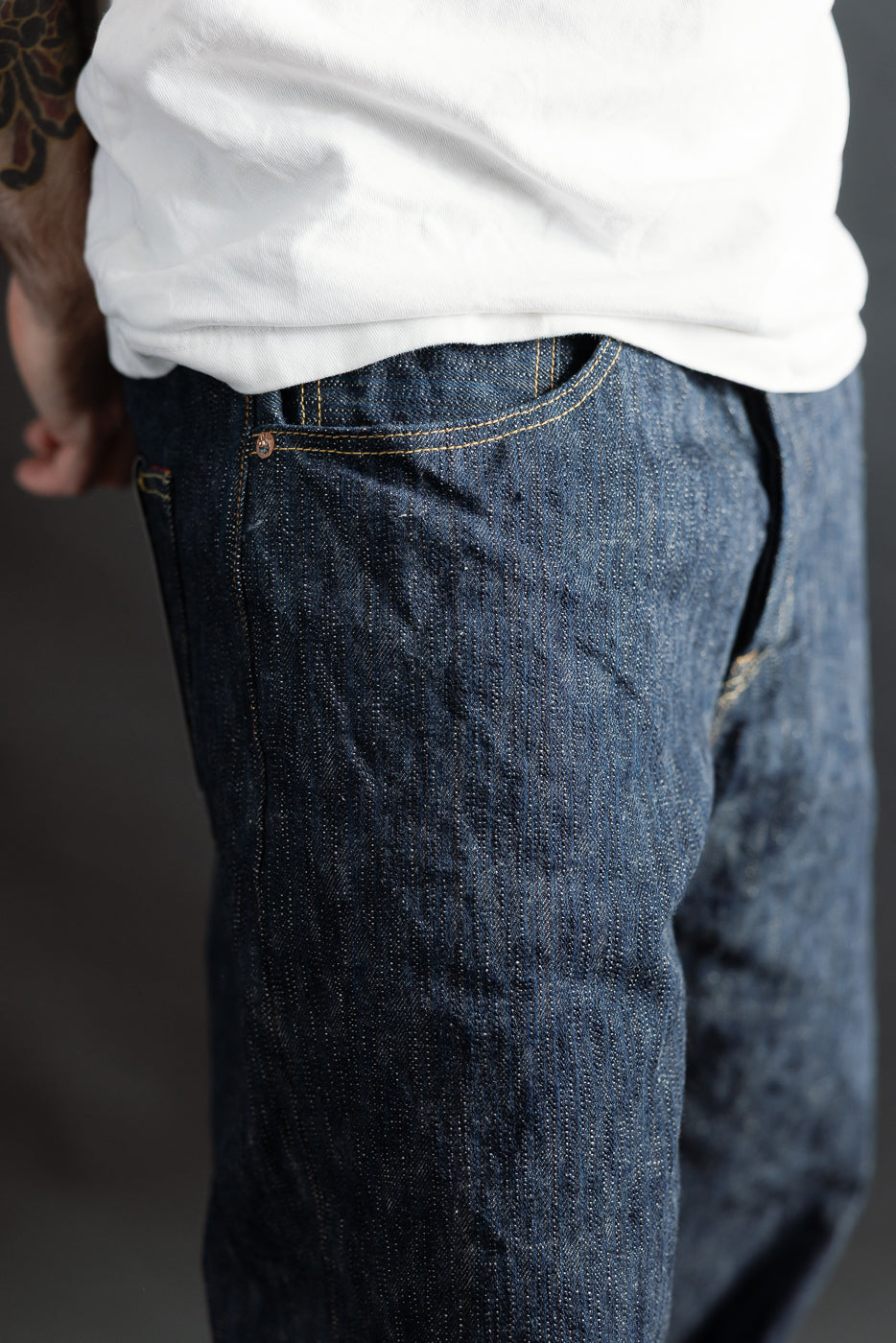 Close-up of front left side of ONI Kase denim selvedge jeans on male model, showing pocket detail and textured indigo fabric. Model is 5'9