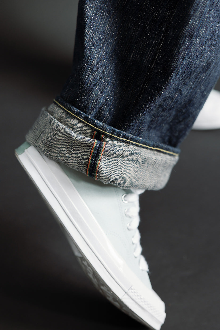 Close-up of selvedge cuff detail on ONI Kase denim jeans, model male, with sneaker, side view.