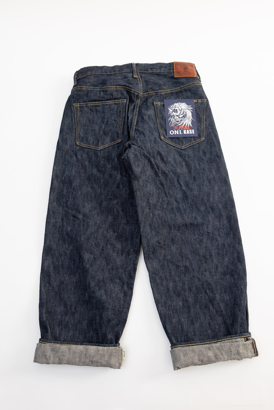 Back view flat lay of ONI KASE 16oz selvedge denim jeans, rear pockets, leather patch, cuffed hem.