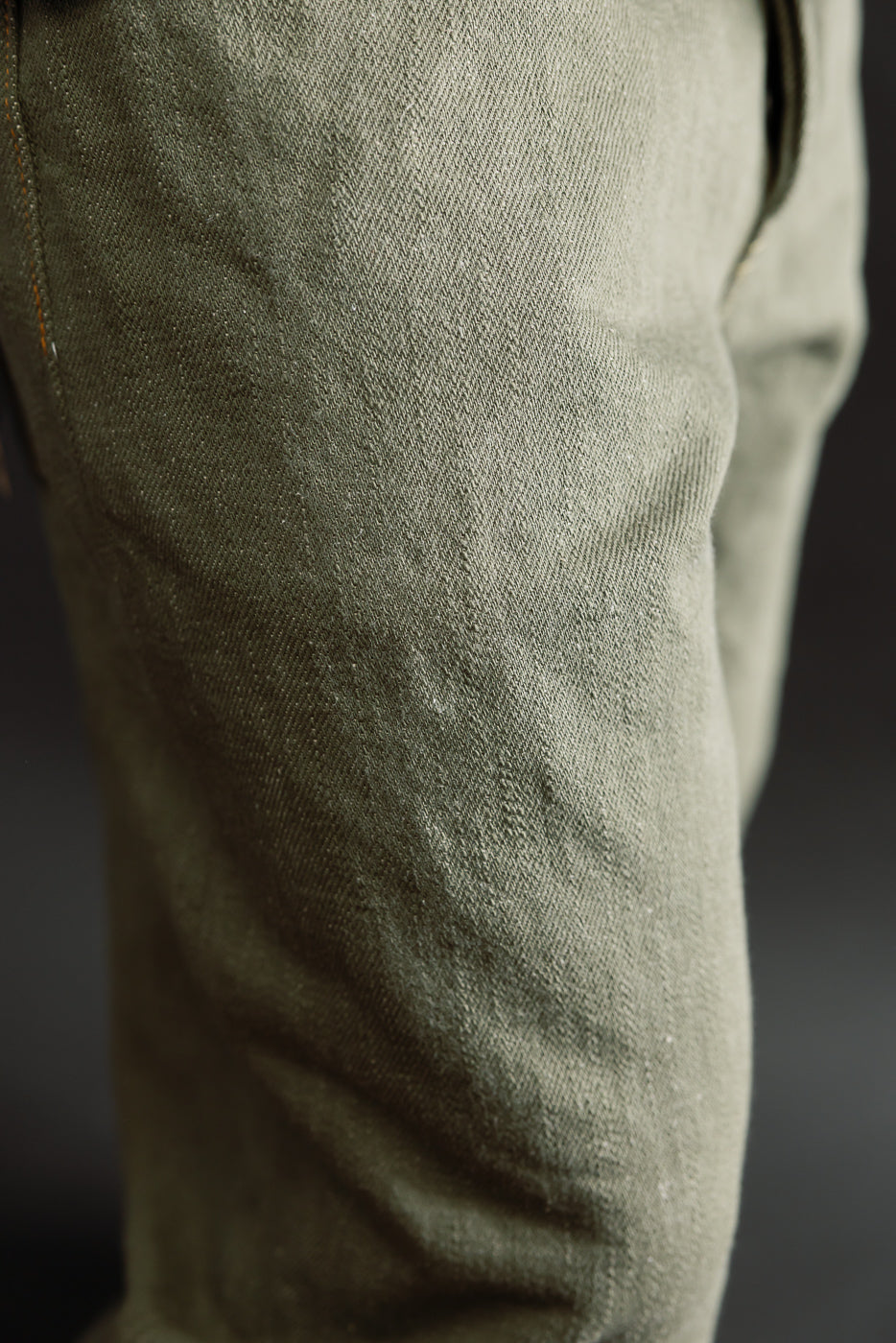 Close-up of olive selvedge denim jeans fabric, thigh area, showing texture and weave.
