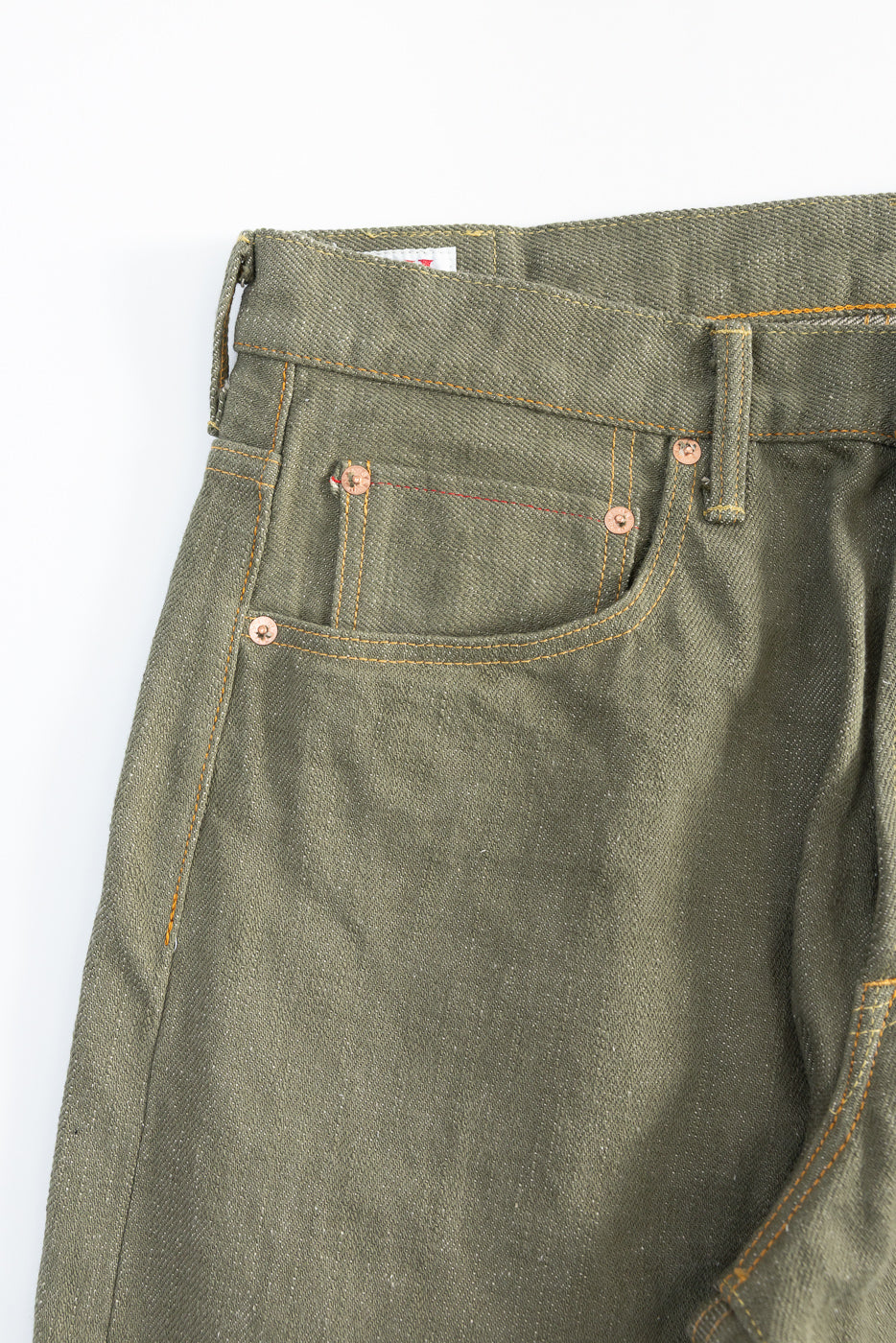 Close-up of front left waist and pocket detail on olive green selvedge denim jeans.