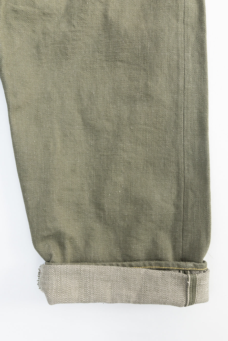 Close-up of olive selvedge denim jeans cuff, showing fabric texture and hem detail.