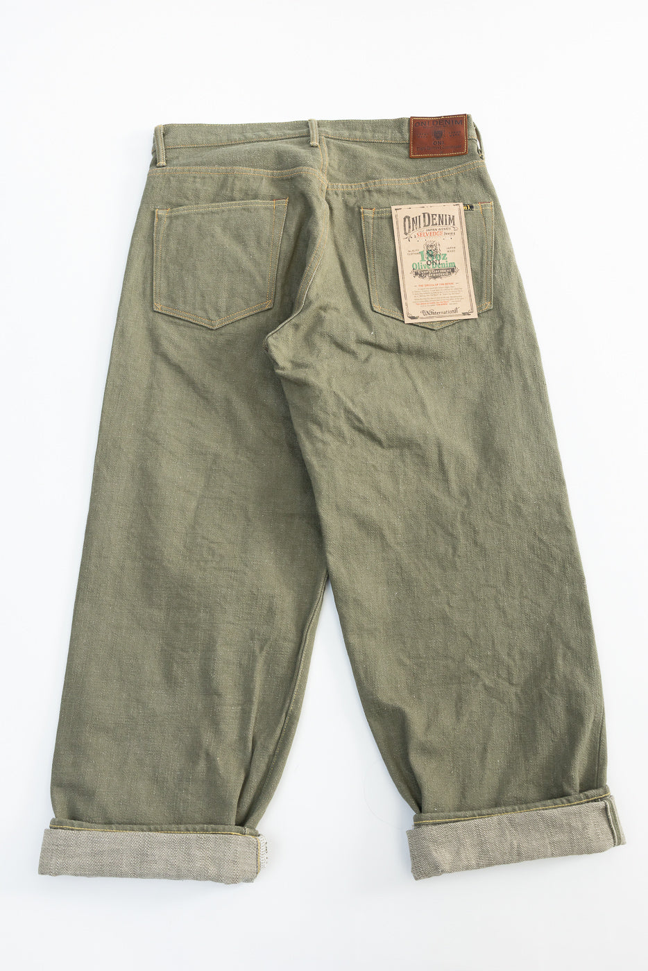 Flat lay of olive green selvedge denim jeans, back side, showing pockets, labels, and cuffed hems.