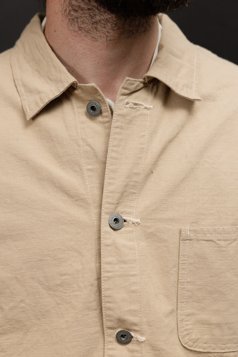 Close-up front view of male model wearing beige work shirt with metal buttons, collar, and chest pocket
