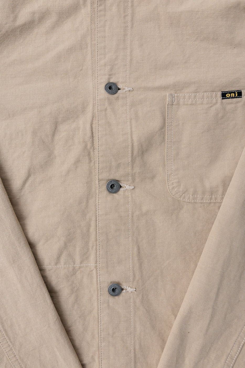 Close-up front view of beige work shirt: button placket, chest pocket, and 'oni' tag detail