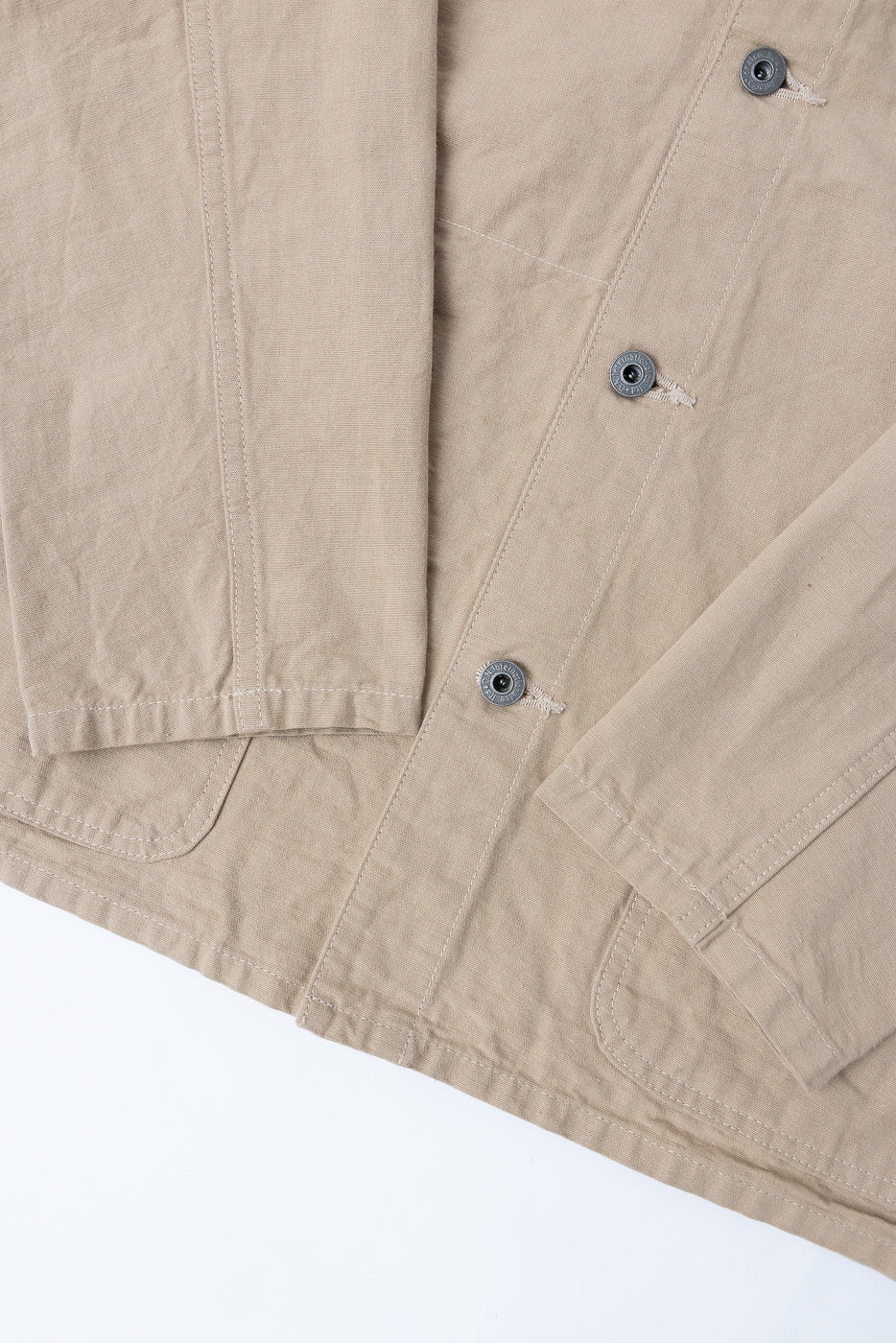 Close-up front view of beige jacket with metal buttons and textured fabric, showcasing sleeve and pocket details.