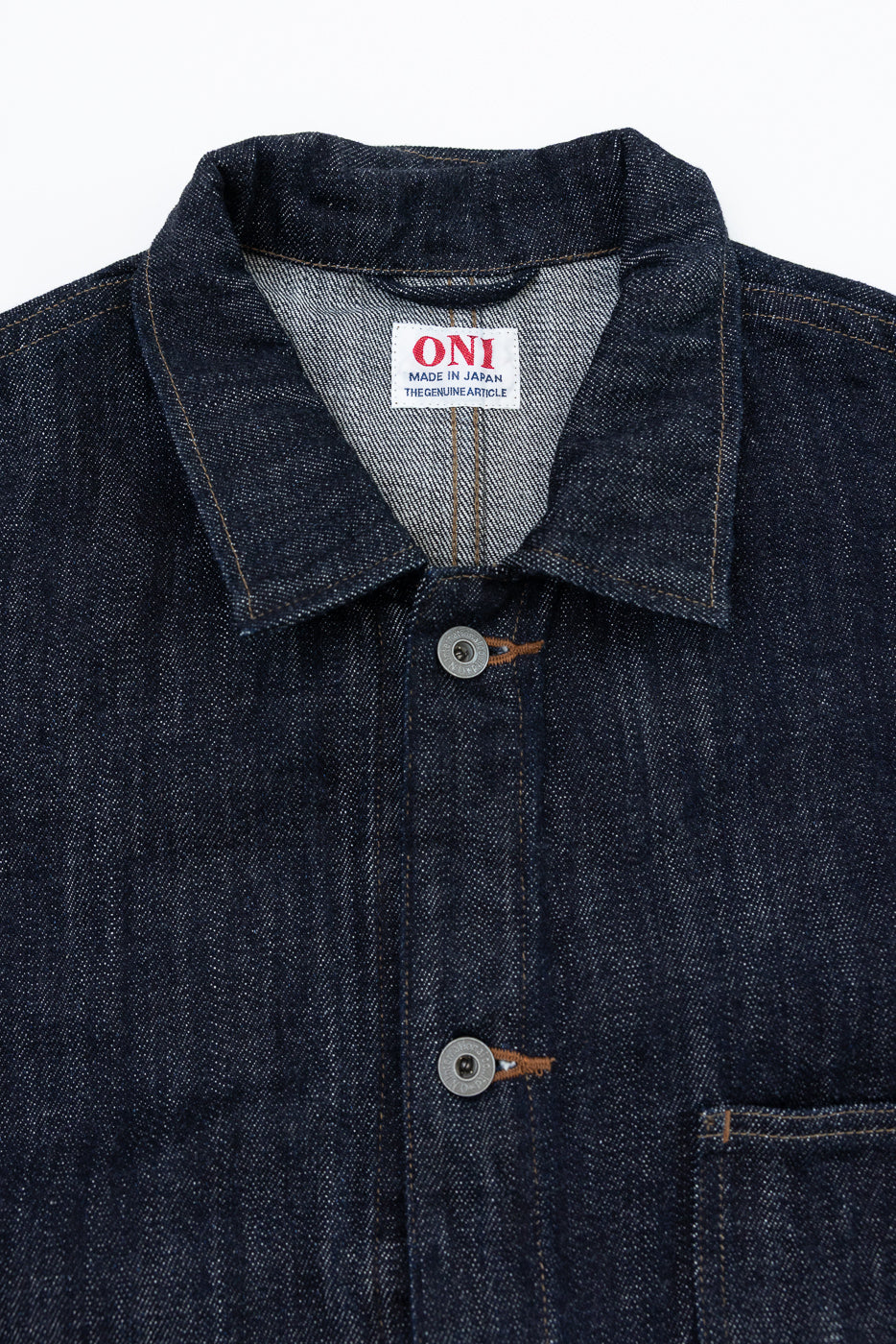 Close-up front view of dark denim jacket showing collar, ONI tag, buttons, and selvedge fabric texture