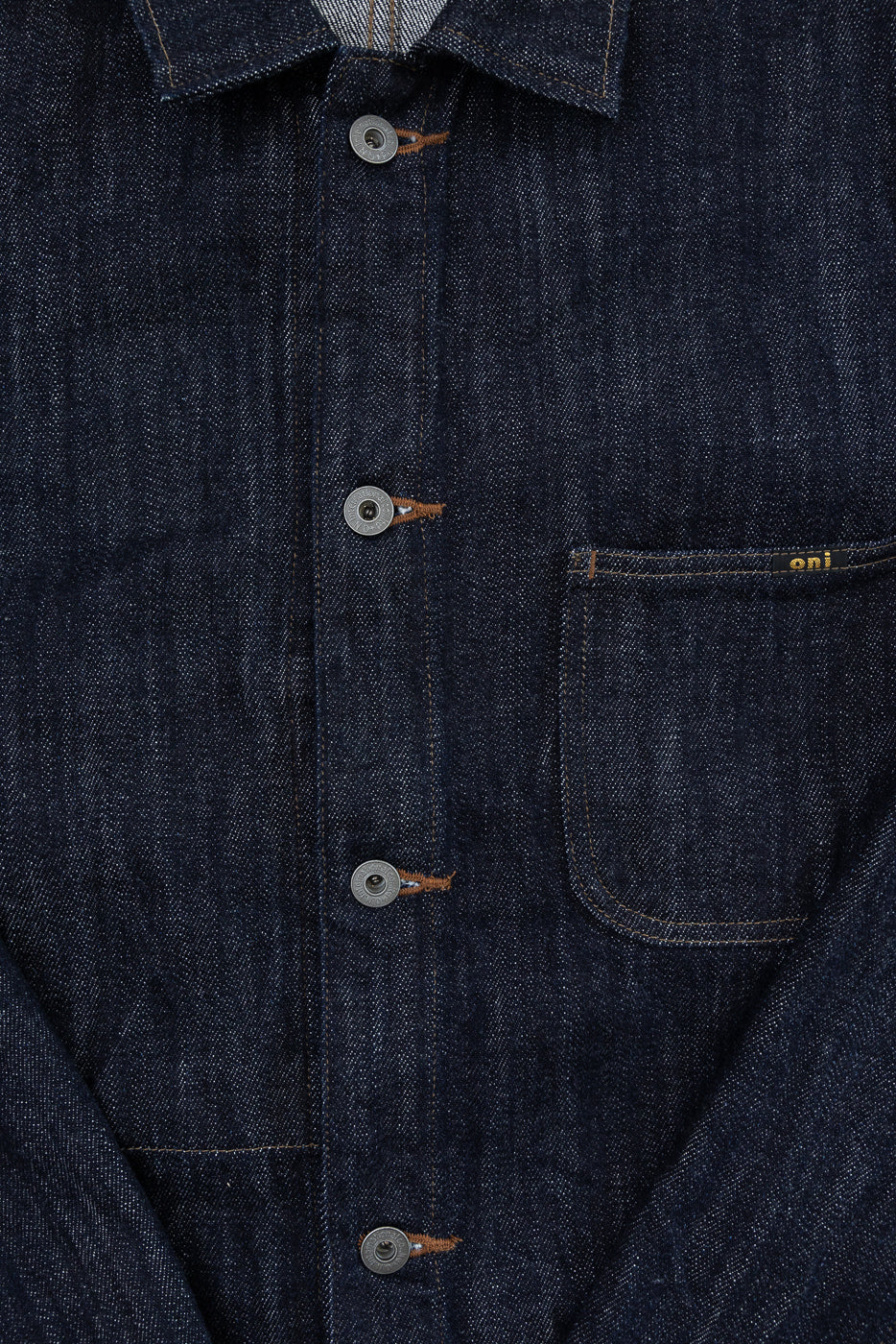 Close-up front view of dark selvedge denim shirt with metal buttons, chest pocket, and 'oni' tag detail