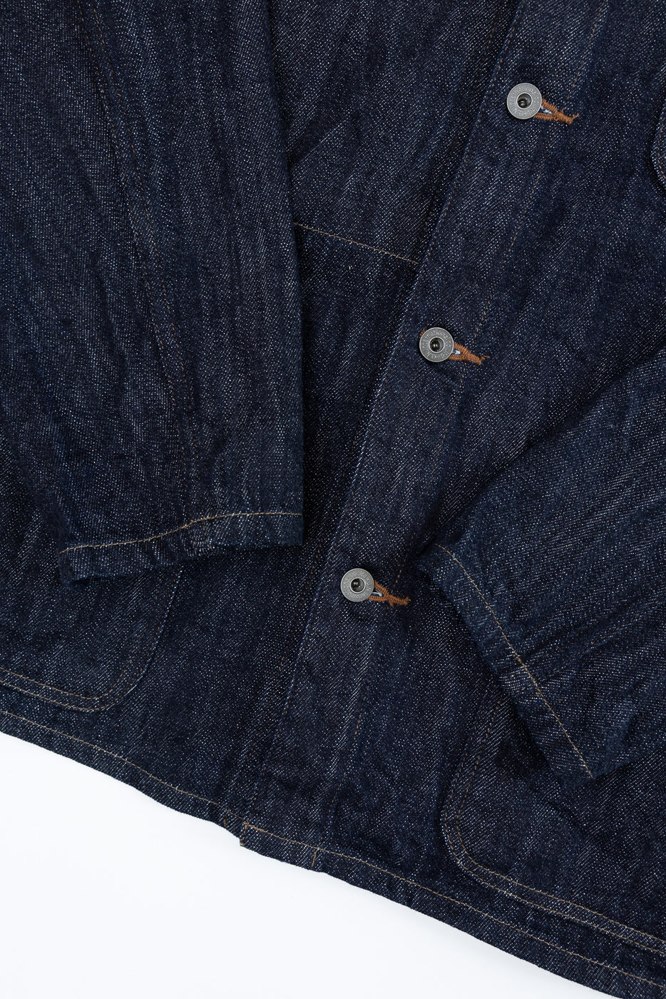 Close-up front view of dark denim jacket showing button placket, selvedge stitching, and fabric texture