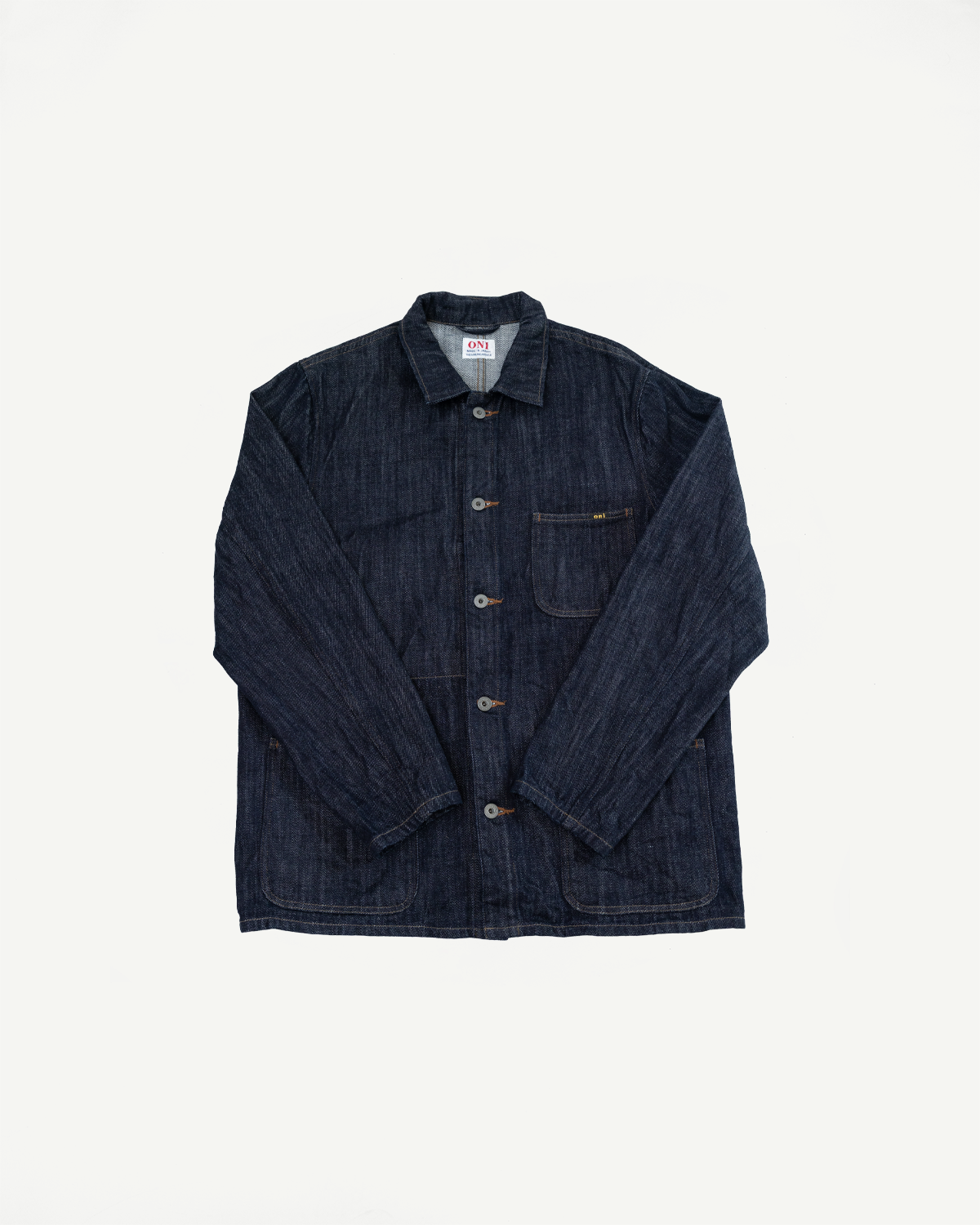 Dark indigo selvedge denim chore coat, front flat lay, button-front, chest pocket, ONI tag visible