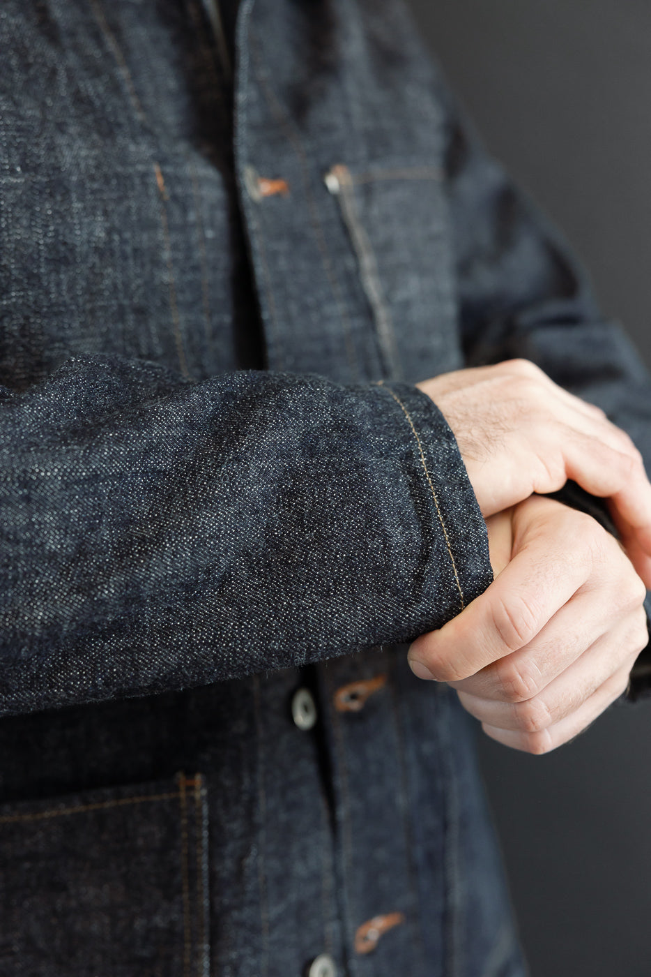 Close-up of male model's arm showing dark denim jacket sleeve, button details, and fabric texture