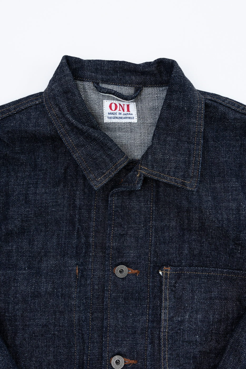 Close-up front view of dark selvedge denim jacket, showing collar, button placket, chest pocket, and ONI brand tag.