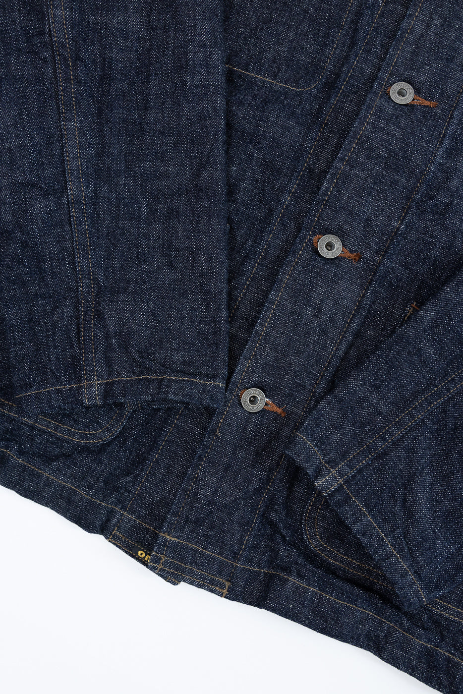 Close-up front view of dark selvedge denim jacket showing button placket, copper stitching, and fabric texture