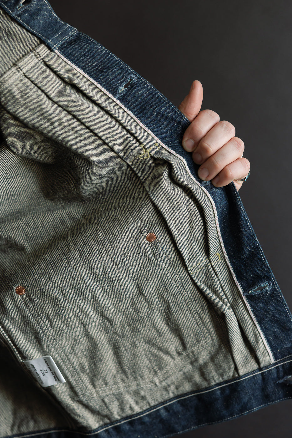 Close-up of interior front panel of selvedge denim jacket, showing pocket rivets, seam details, and fabric texture.