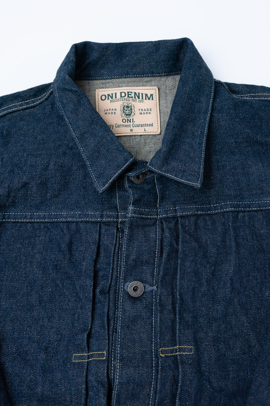 Close-up of front upper chest and collar of a selvedge denim jacket, showing tag, buttons, and texture.